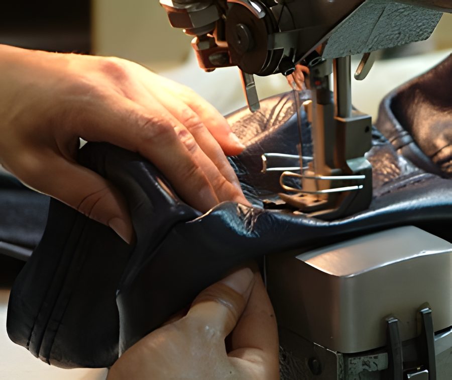 Deux mains guident un cuir noir sous l'aiguille d'une machine à coudre industrielle