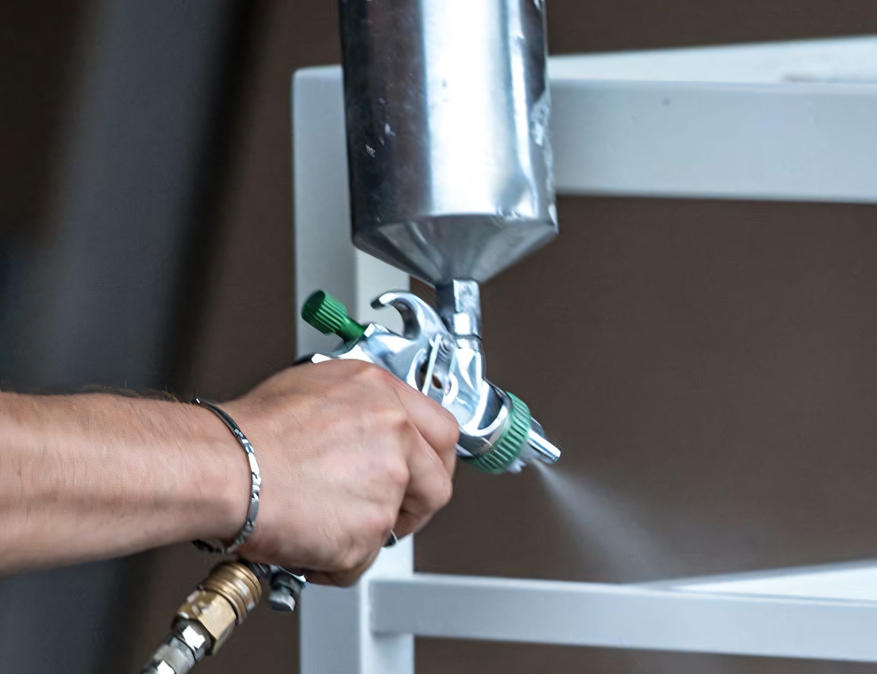 Un pistolet à peinture en main, un peintre de meubles applique la finition sur une structure de bois blanche
